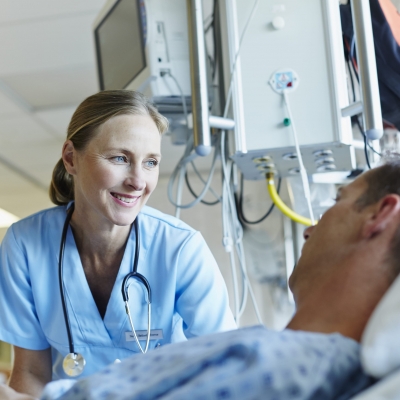 A nurse navigator coordinates appointments and treatment options with a cancer patient who is lying in bed