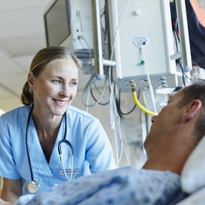 A nurse navigator smiles as she explains the support groups and resources available at Florida Hospital to a cancer patient who is lying in bed