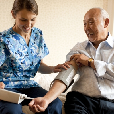 A cancer care specialist checks the blood pressure of an older man in a button-down shirt