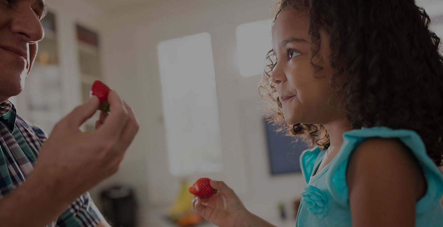 A childhood cancer survivor and father eat strawberries in their kitchen