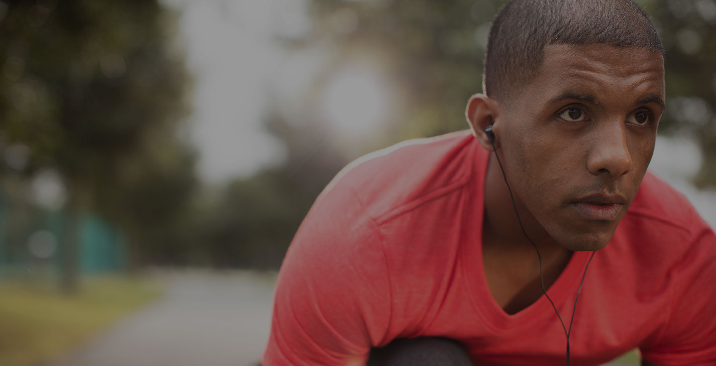 A prostate cancer survivor in a red shirt enjoys life after cancer by working out in a park while wearing headphones