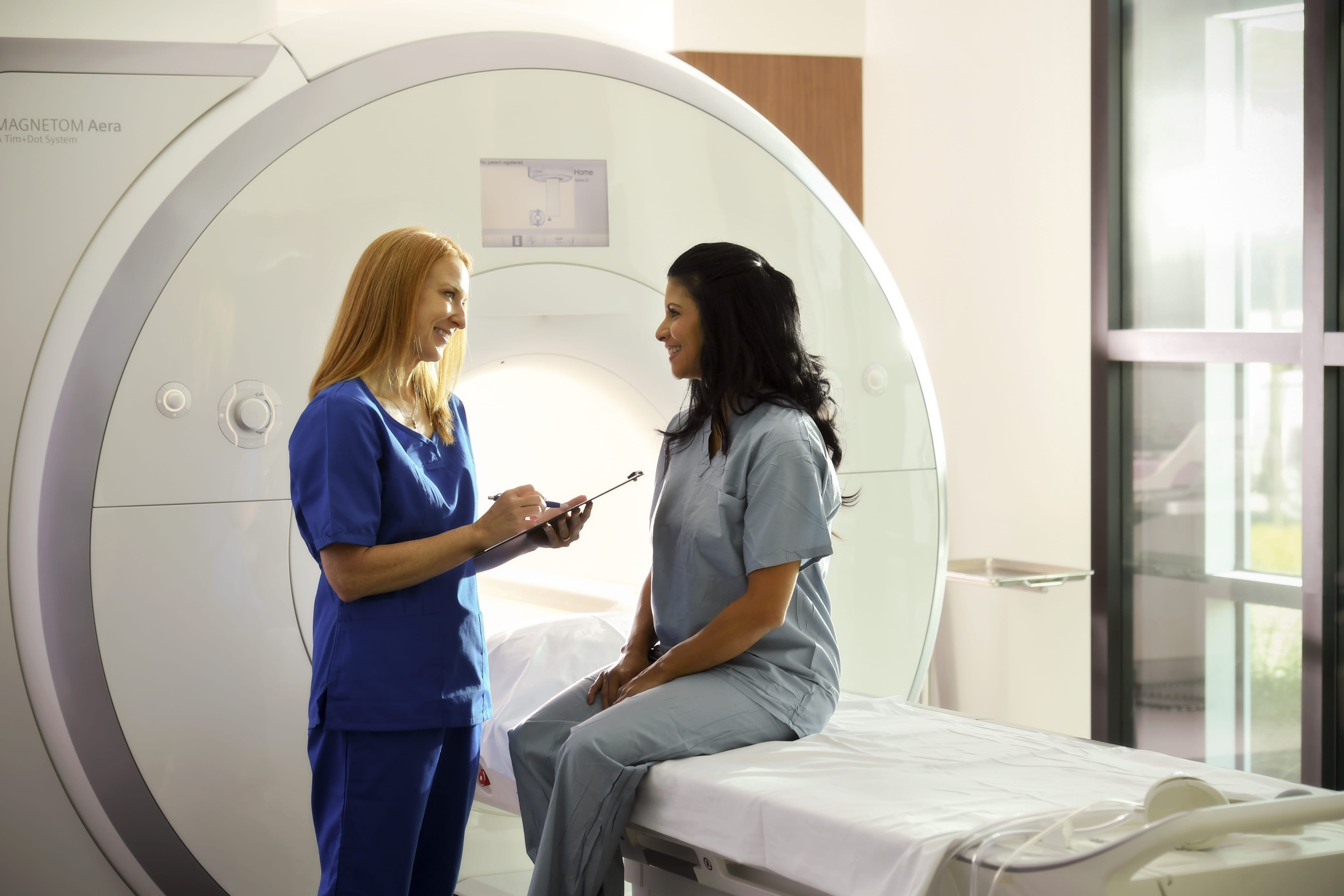 A bone marrow transplant patient and cancer care specialist talk in front of an CT scan machine