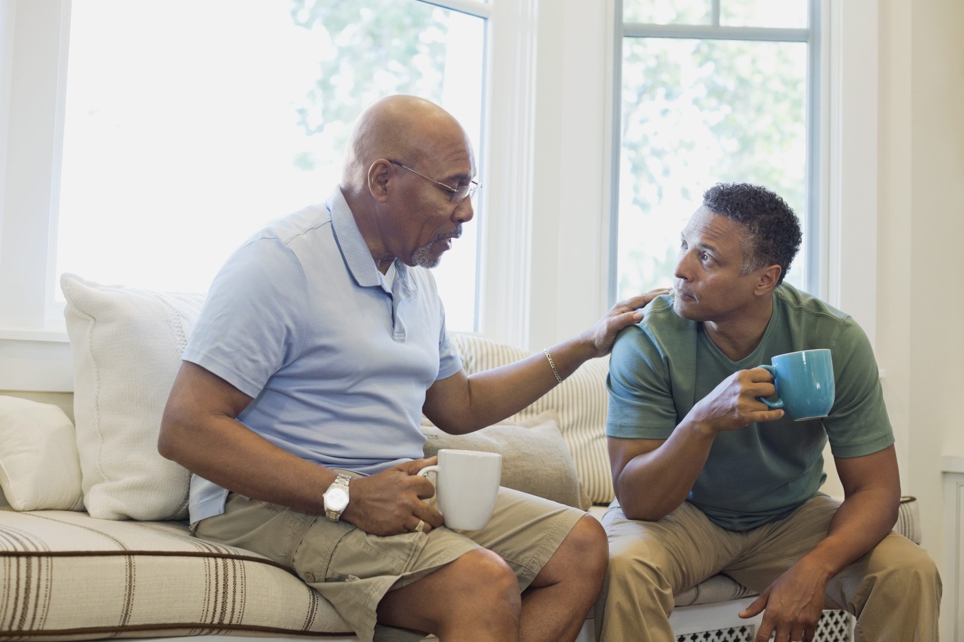 Two men drinking coffee discuss brain cancer support groups in a well lit living room