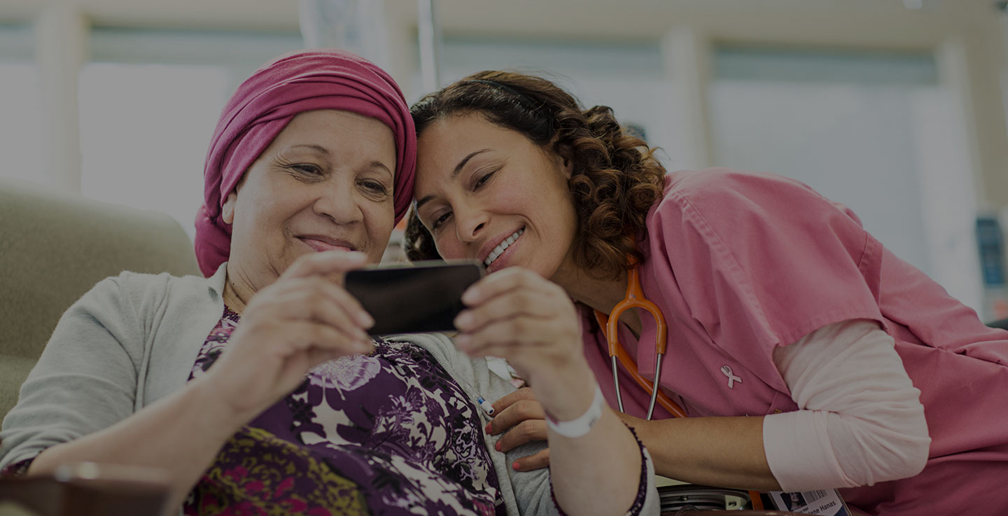 A chemotherapy patient and a cancer treatment specialist smile as they look at photos on a phone together