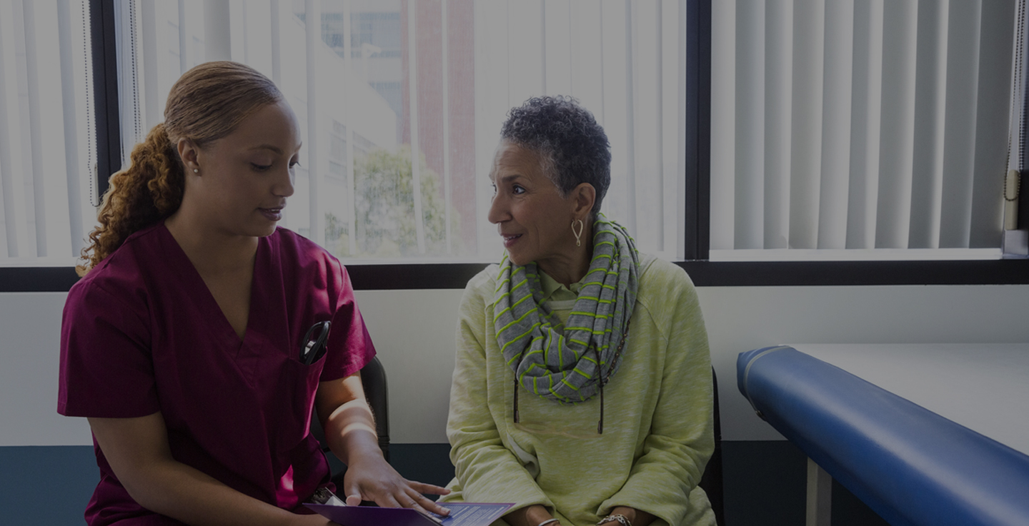 A cancer care specialist dressed in scrubs and a cancer patient in a green shirt discuss patient education tools