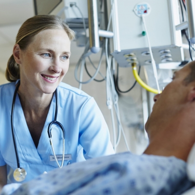 An oncologist smiles as she speaks with a cancer treatment patient who lying in bed 