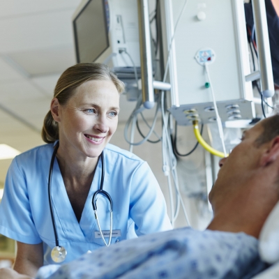 A nurse navigator smiles as she explains cancer screening and prevention options with a patient who is lying in bed