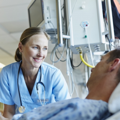 A nurse navigator smiles as she guides a patient who is lying in bed through Florida Hospital's advanced surgical oncology program